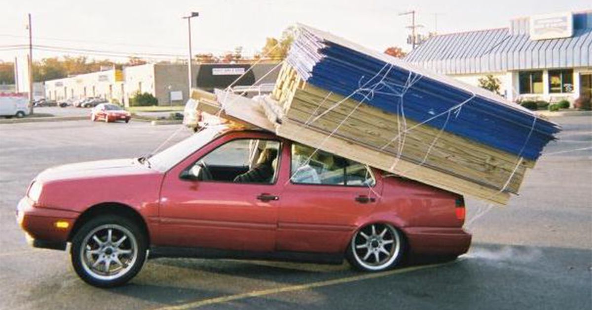 AppImage software delivery meme: Volkswagen Jetta with collpased tires and suspension due to a ton of 4’ x 8’ chip board sheets strapped to it’s roof